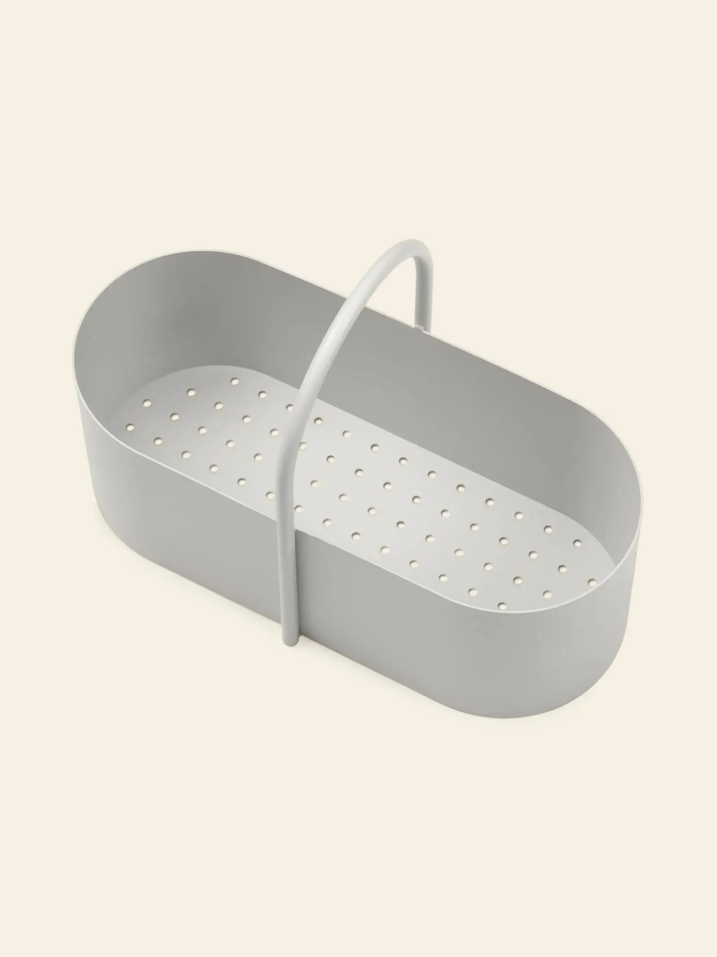 The ferm LIVING Grib Toolbox by ferm LIVING, a light gray, oval-shaped plastic container with a slim design and single arched handle, featuring multiple holes at the bottom, is displayed on a plain beige background.