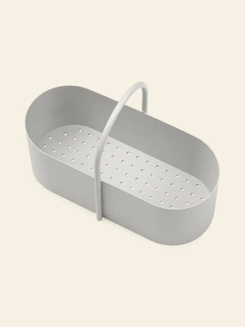 The ferm LIVING Grib Toolbox by ferm LIVING, a light gray, oval-shaped plastic container with a slim design and single arched handle, featuring multiple holes at the bottom, is displayed on a plain beige background.