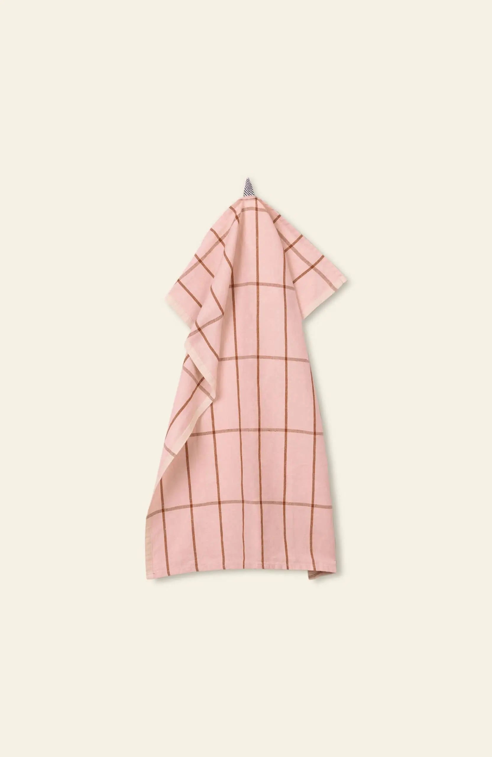 The ferm LIVING Hale Tea Towel by ferm LIVING, featuring a pink and brown grid pattern, hangs from a small loop against a light beige background.