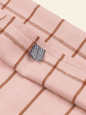 A close-up of the ferm LIVING Hale Tea Towel shows pink fabric with brown checks and a small navy and white striped tab sewn into the seam.