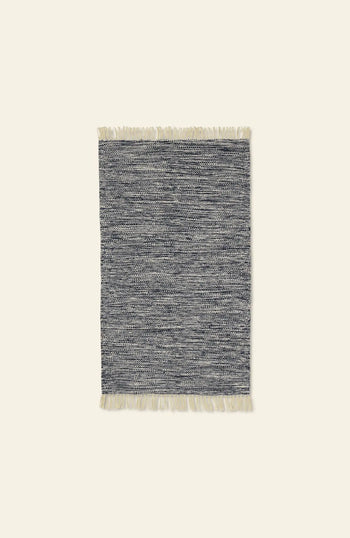 The ferm LIVING Melange Rug by ferm LIVING features a rectangular shape in gray and white with a textured pattern and short cream fringe on the ends, providing an easy-care, luxurious look, shown against a plain light background.