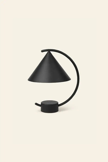 The ferm LIVING Meridian Lamp by ferm LIVING is a modern black lamp with a sculptural design, featuring a conical shade and curved arm on a circular base, shown against a plain beige background.
