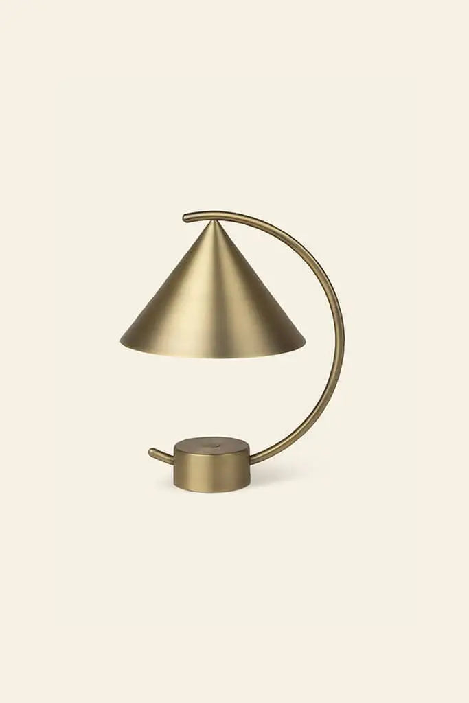 The ferm LIVING Meridian Lamp by ferm LIVING features a sculptural brass design with a conical shade and curved arm, set against a light beige background. Its minimalist, contemporary lines lend an elegant, modern touch.
