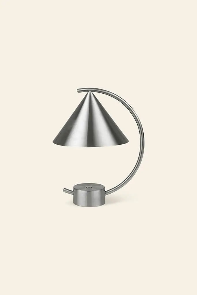 The ferm LIVING Meridian Lamp by ferm LIVING is a modern, minimalist desk lamp with a conical shade and curved arm, crafted from powder coated steel and set against a light beige background.