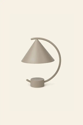 The ferm LIVING Meridian Lamp by ferm LIVING is a modern minimalist table lamp with a sculptural form, conical shade, and curved arm in smooth beige powder-coated steel, shown against a plain light background.