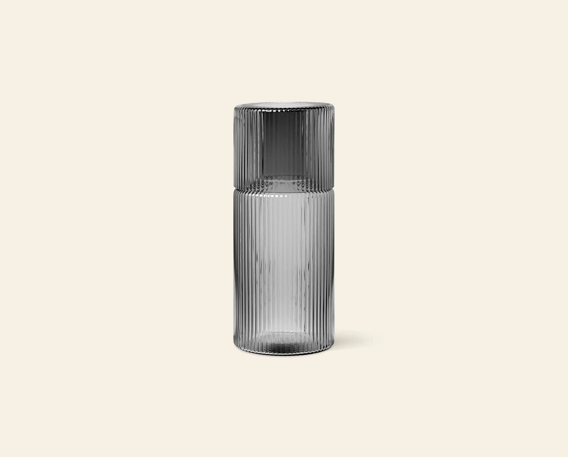 The ferm LIVING Ripple Carafe Set, Small features a transparent ribbed glass carafe with a matching cup that sits upside down on top, both crafted from mouth-blown glass and shown against a plain beige background.