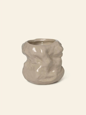 The ferm LIVING Tuck Scented Candle by ferm LIVING features an uneven, organic shape in light beige ceramic, creating a calming ambiance when displayed against a plain, off-white background.