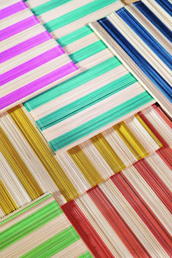 A geometric close-up of &klevering Bay Placemats, Set of 6, overlapping in vibrant summer hues with cream and colored stripes—green, blue, pink, yellow, orange, and red—arranged in a layered pattern.