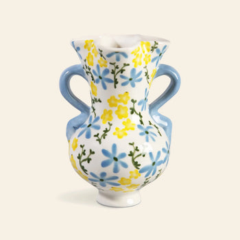 The &klevering Buttercup Vase by &klevering features a classic curvy shape with two blue handles, a flared rim, and hand-painted blue and yellow petite flowers with green stems on a white ceramic background.
