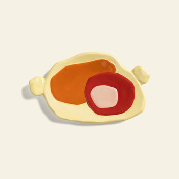 The &klevering Chunky Platter, Small, is a ceramic plate with bold abstract orange, red, and pink at the center, two uneven side handles, and a plain off-white background—ideal for those who love artistic charm.
