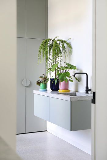 A modern, minimalist bathroom features a floating gray vanity with a black faucet, topped with the cheerful &klevering Churros Planter for a pop of color against white walls and tall gray cabinets.
