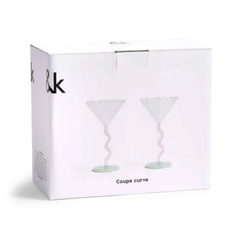 A white box displays two &klevering Curved Coupe Glasses—elegant, wavy pink stems and wide bowls—ideal for celebrations. “Coupe curve” is printed below the glass images. Set of 2 by &klevering.