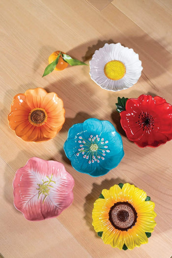 Six colorful &klevering ceramic bowls, including the Daisy Bowl, are arranged on a light wooden surface with a small orange ornament and green ribbon—perfect for adding cheer to your summer picnic or garden dinner.