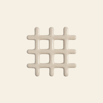 The &klevering Grid Trivet by &klevering features a shiny off-white, speckled grid design that resembles icing on a light beige background. This stylish trivet adds visual appeal while protecting surfaces from heat.