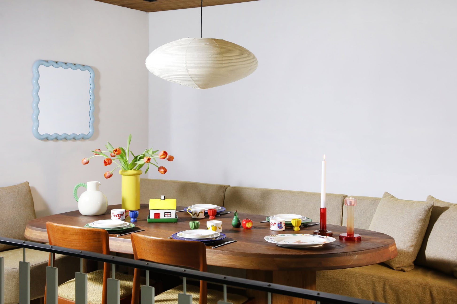 A cozy dining area with a round wooden table set for four, featuring decorative tableware and the &klevering Haines Apple Pear Salt & Pepper Set, plates, cups, a candle, orange tulips, and playful accents for a fun, functional design.