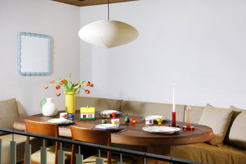 A cozy dining area with a round wooden table set for four, featuring decorative tableware and the &klevering Haines Apple Pear Salt & Pepper Set, plates, cups, a candle, orange tulips, and playful accents for a fun, functional design.