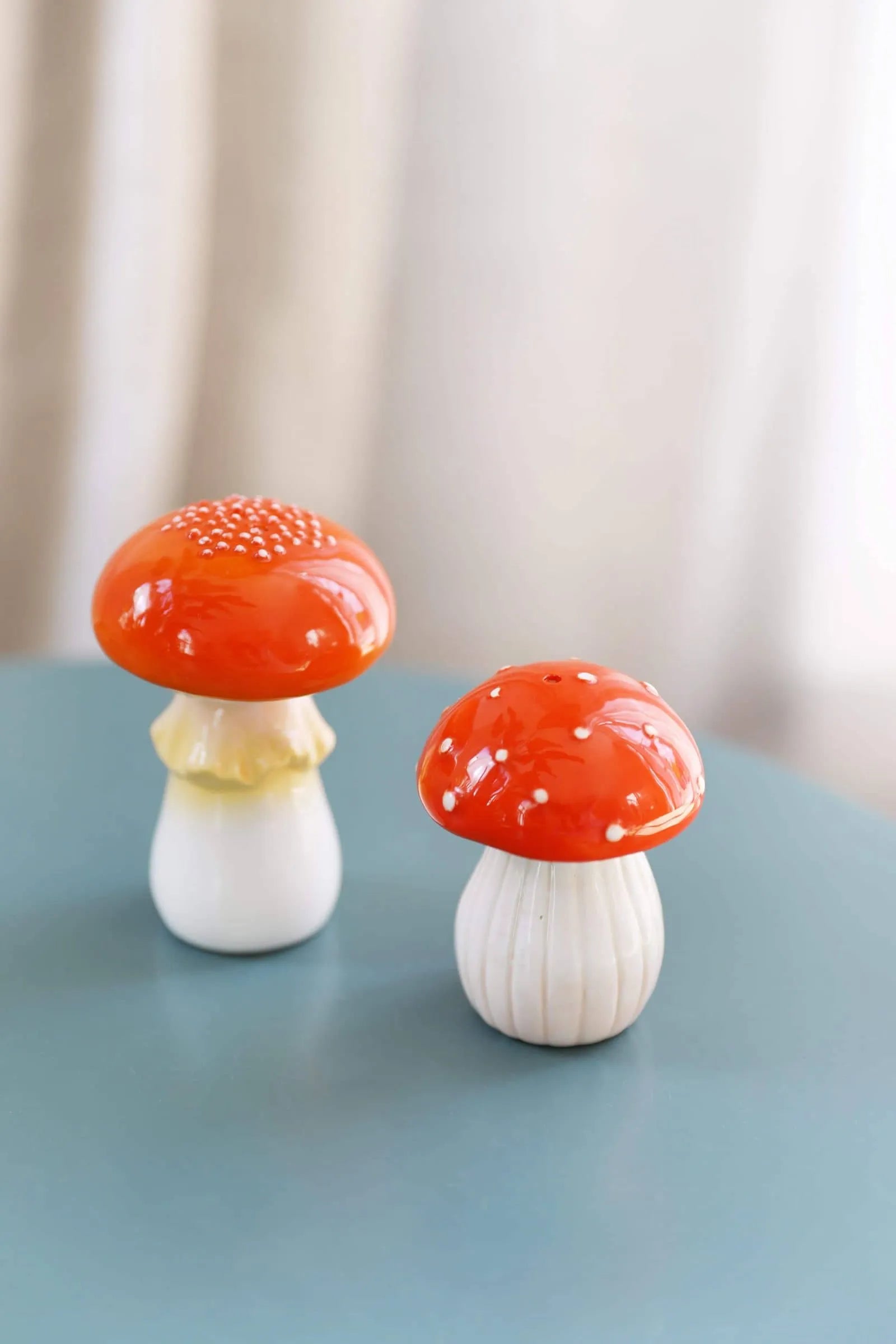 The &klevering Mushroom Salt & Pepper Set features two ceramic figurines with red caps and white stems, one with a wide dotted cap and the other taller with a yellow-tinted stem—perfect for whimsical kitchen decor.