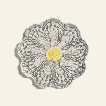 The &klevering Oyster Plate by &klevering is a decorative gray ceramic plate shaped like layered oyster shells with detailed ridges and a central yellow lemon wedge design—ideal for serving oysters. Photographed on a plain, light background.