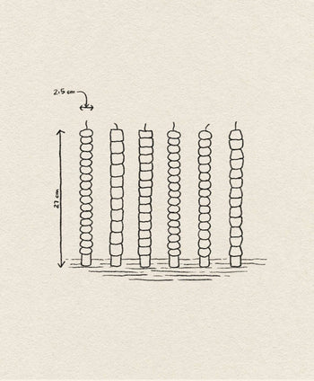 A hand-drawn illustration showcases the &klevering Pebble Candle Set of 6, each 21 cm tall and spaced 2.5 cm apart, with unique color accents—evoking handcrafted charm on a textured surface.