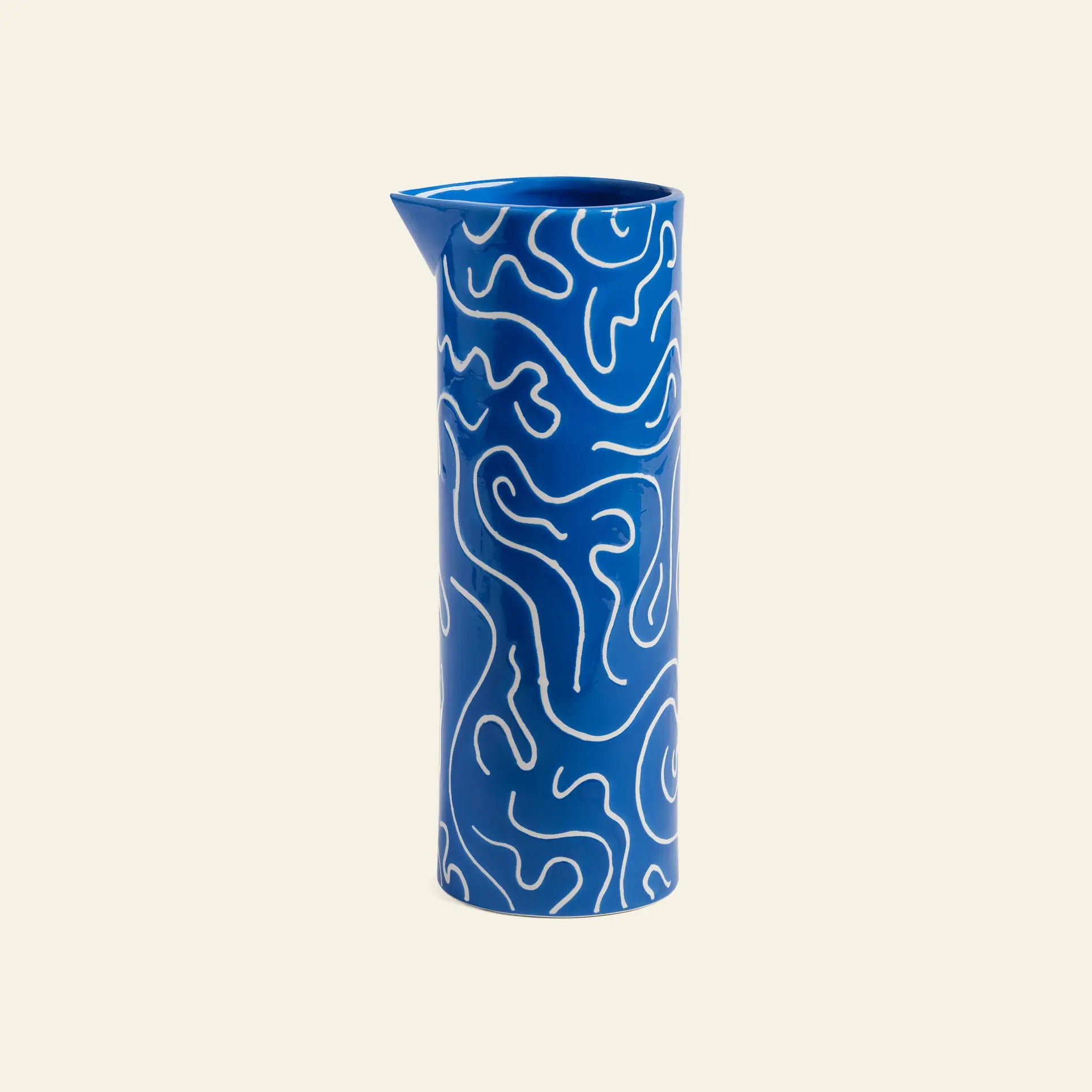 The &klevering Soba Jug is a tall vessel in bold blue, adorned with playful white squiggle doodles and a small spout, displayed against a plain light background.