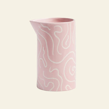 The &klevering Soba Jug is a pink ceramic jug with a glossy finish, decorated with cheerful white doodle prints and wavy abstract lines, all set against a light beige background.
