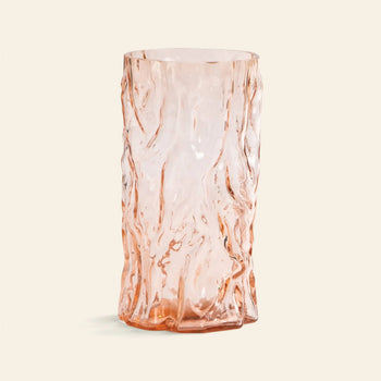 The &klevering Trunk Vase by &klevering is a tall, pale pink glass vase with a translucent finish and an irregular, organic surface that resembles melted or crumpled material, displayed against a plain light background.