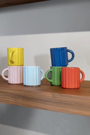 Six &klevering Tube Mugs, a set of 6 in vibrant yellow, pink, blue, green, red, and dark blue, are shown both stacked and arranged side by side on a wooden shelf.