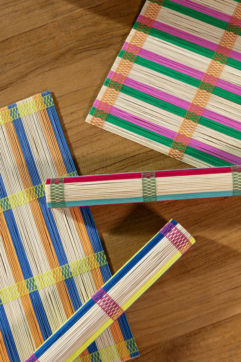 The &klevering Umami Placemat Set of 4 features colorful striped bamboo designs in blue, green, orange, pink, and yellow—two rolled up and two flat—ideal for adding vibrant style to your dining table.