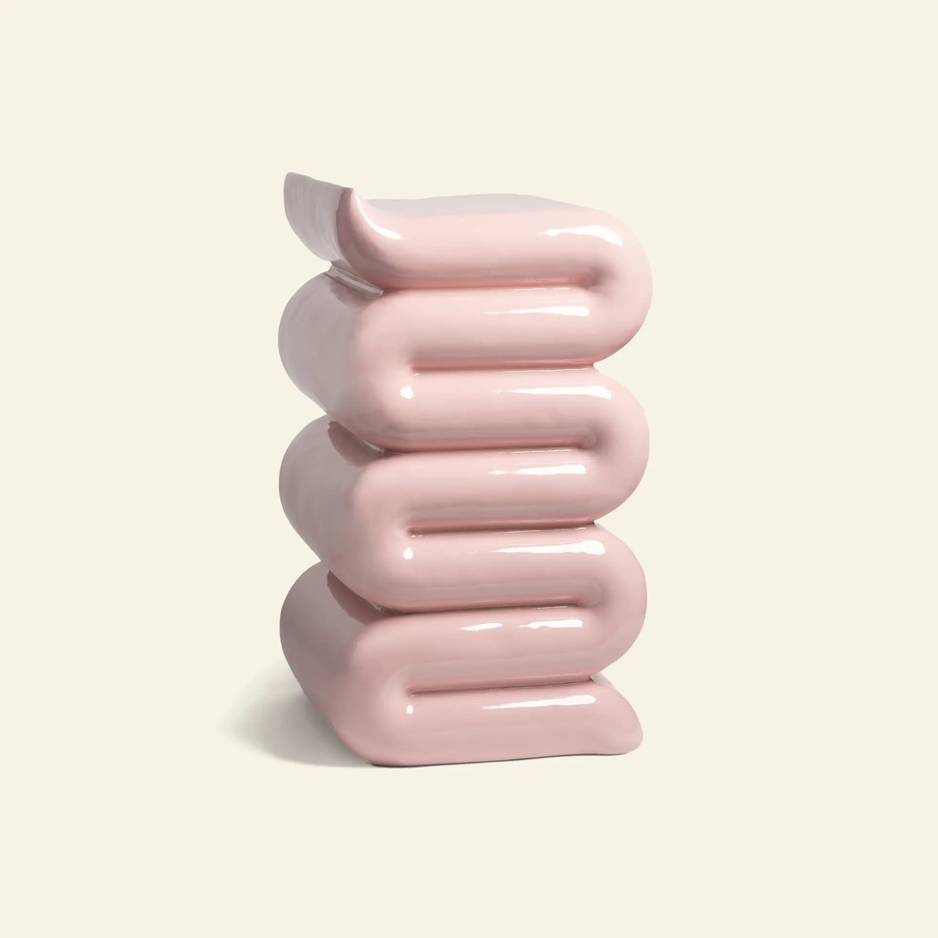 The &klevering Whip Pillar - Pink by &klevering, with its shiny pastel surface and stacked, folded design reminiscent of curved ribbons or soft cushions, stands against a plain off-white background.