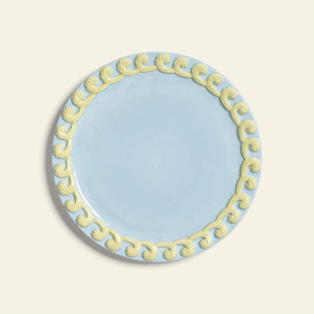 The &klevering Whipped Plate, Set of 4, features light blue plates with decorative yellow swirls along the rim, inspired by candy colors and displayed against an off-white background.