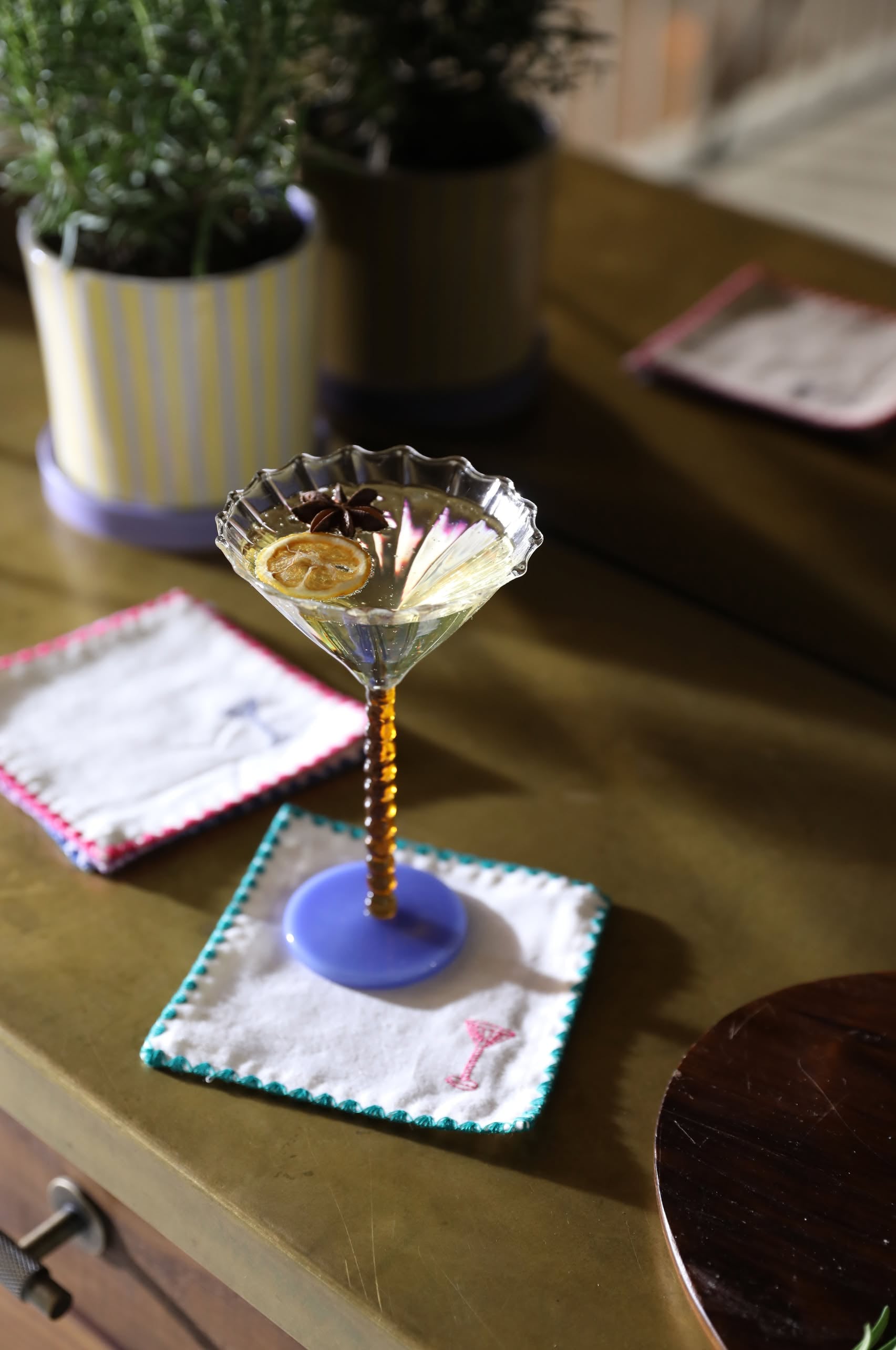 A cocktail garnished with dried citrus and star anise sits on the &klevering Zigzag Cocktail Napkin (Set of 4) with vibrant embroidery atop a brass table—ideal for adding style to any gathering.