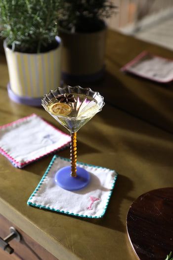 A cocktail garnished with dried citrus and star anise sits on the &klevering Zigzag Cocktail Napkin (Set of 4) with vibrant embroidery atop a brass table—ideal for adding style to any gathering.