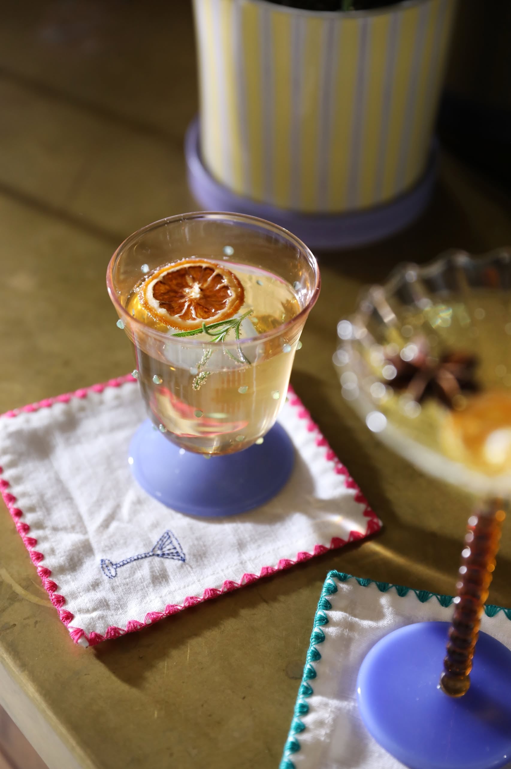 A clear drink with a dried orange slice and herbs rests on an &klevering Zigzag Cocktail Napkin, Set of 4—vividly embroidered and ideal for stylish cocktail gatherings.