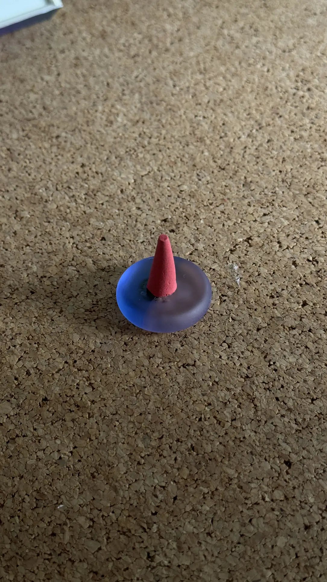 The ripple+ Incense Droplets Multipack (48 Droplets) features a small, cone-shaped incense stick in a translucent purple holder by ripple+, releasing aromatic scents for mood enhancement on any cork surface.
