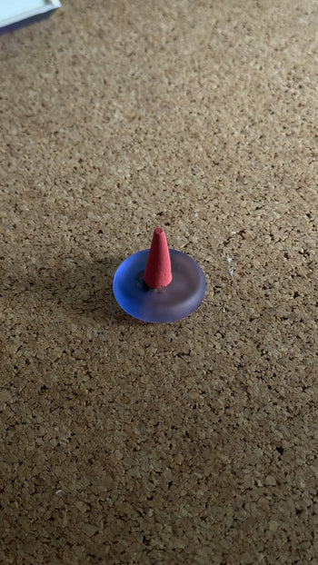 The ripple+ Incense Droplets Multipack (48 Droplets) features a small, cone-shaped incense stick in a translucent purple holder by ripple+, releasing aromatic scents for mood enhancement on any cork surface.