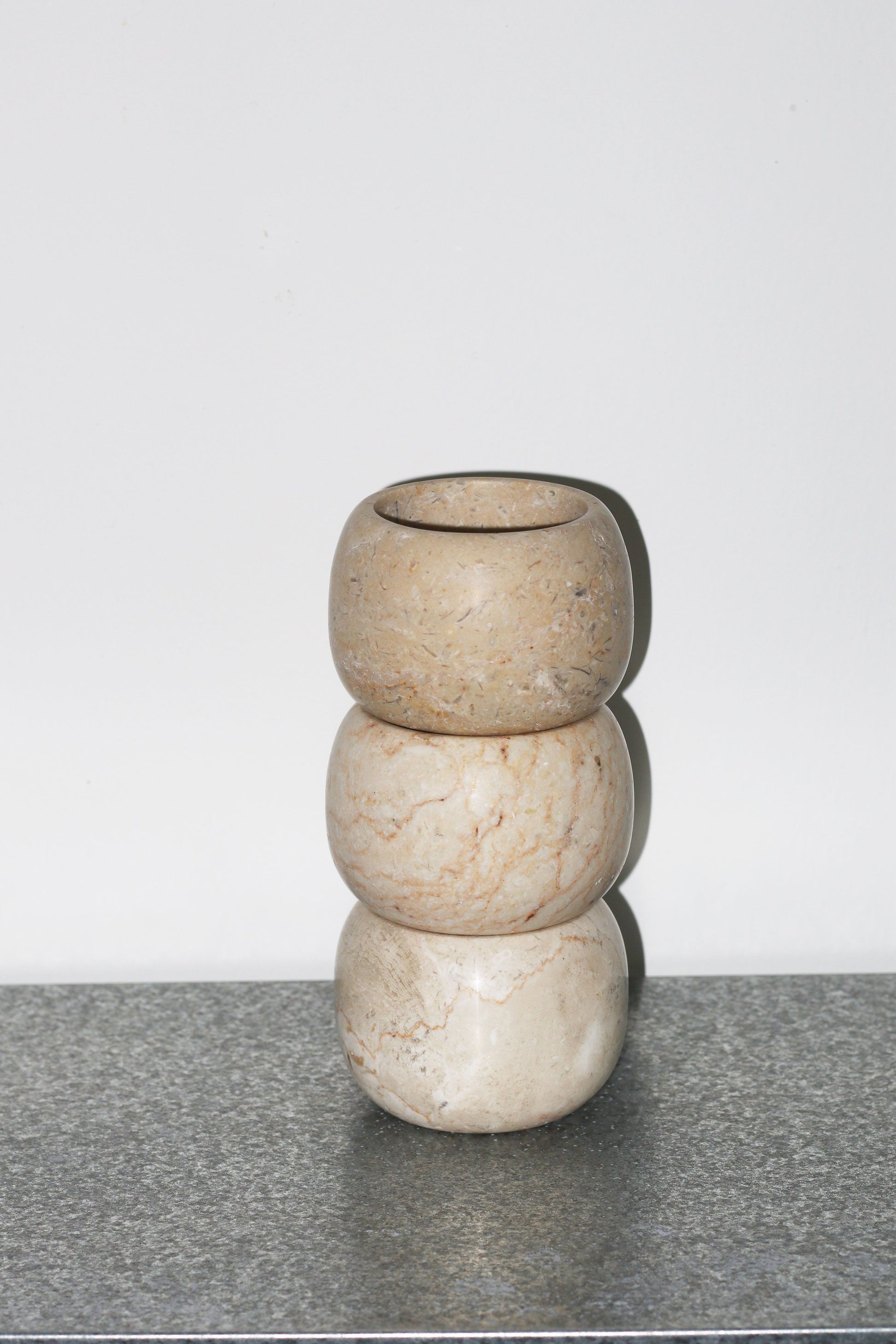 Three round, beige stone stillgoods Abel Duo Holders are stacked atop each other against a plain white background, positioned on a gray speckled surface.