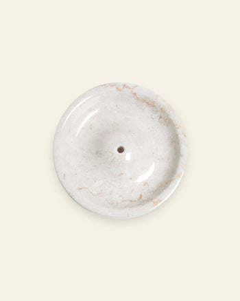The stillgoods Ebb Incense Holder is a round, white marble dish with a subtle marbled pattern and central drainage hole. Shown on a light beige background, it’s perfect as an accessory tray or minimalist incense holder for your space.