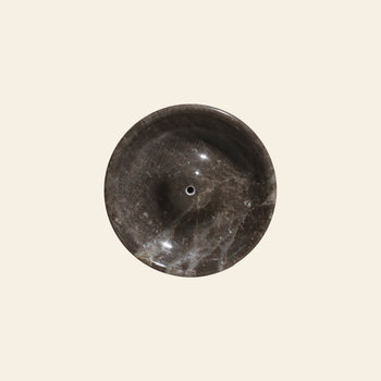 The stillgoods Ebb Incense Holder, a round dark brown marble piece with subtle white veining, is shown from above on a plain beige background—ideal as a striking accessory for your bathroom or vanity.