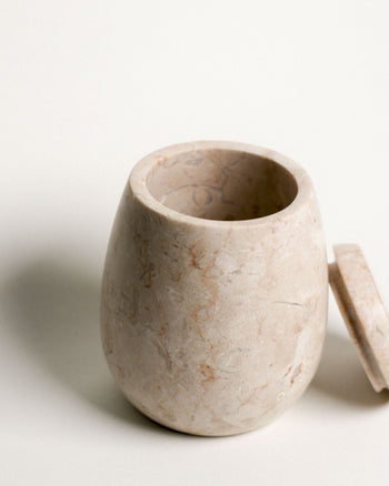 The stillgoods Ecru Jar features a smooth, polished finish with subtle veining. Set on a white surface with its matching lid, this stylish organizer by stillgoods is ideal for storing condiments or adding elegance to your countertop.