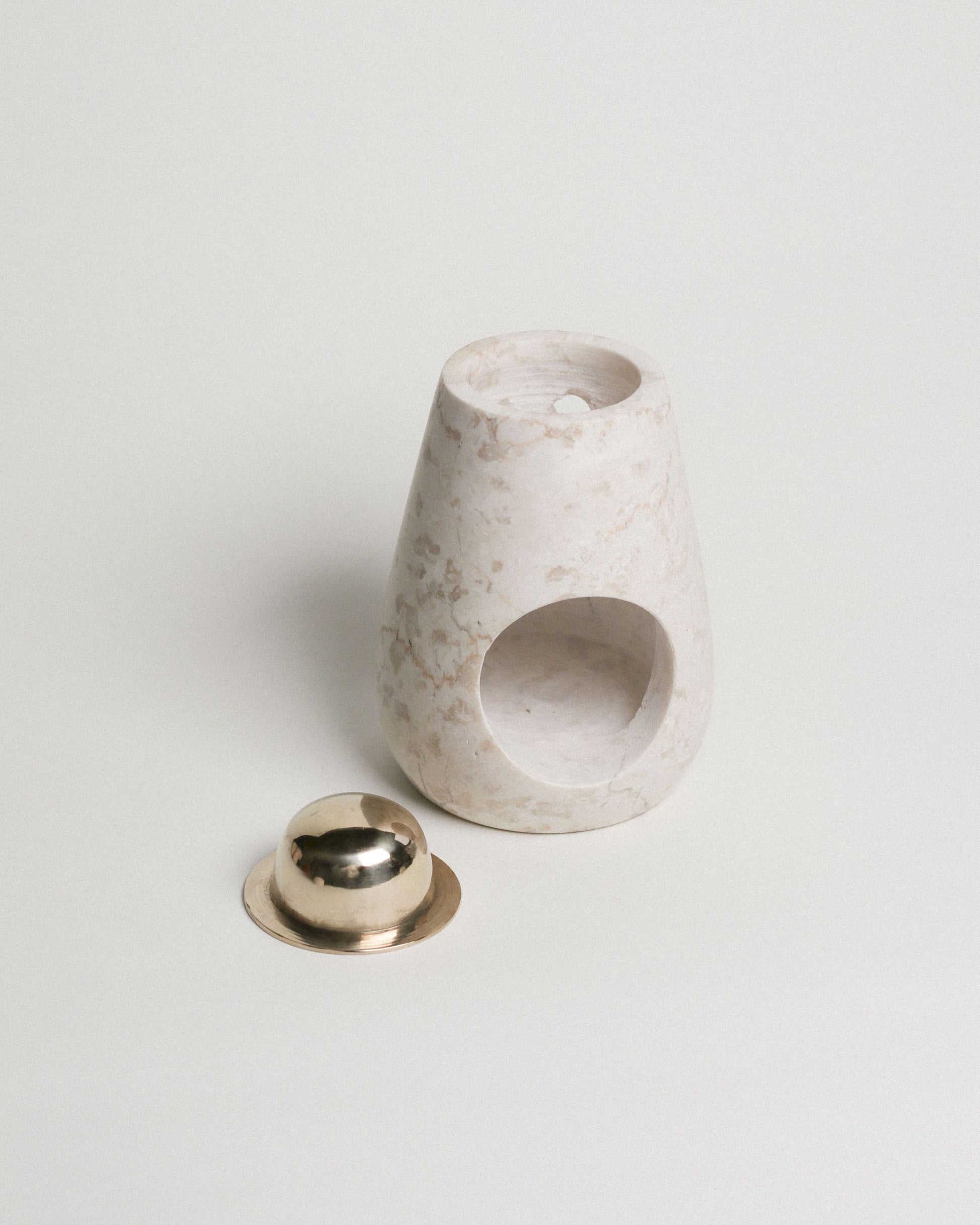 The stillgoods Eli Oil Burner features a minimalist design with a round opening, placed next to a small gold-toned metal dish on a white background—ideal for bringing calming scents to your space.