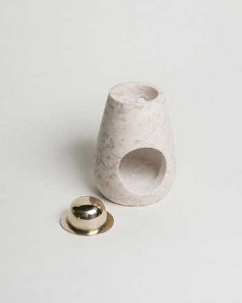 The stillgoods Eli Oil Burner features a minimalist design with a round opening, placed next to a small gold-toned metal dish on a white background—ideal for bringing calming scents to your space.