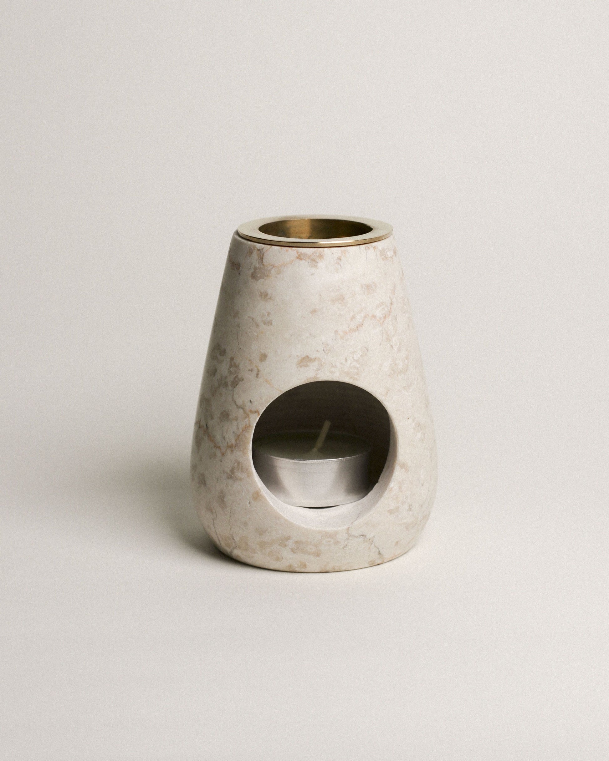 The stillgoods Eli Oil Burner is a marble essential oil diffuser with a rounded conical shape, featuring a front opening for a tealight and a metal bowl on top to diffuse your favorite oils or wax.