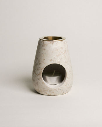 The stillgoods Eli Oil Burner is a marble essential oil diffuser with a rounded conical shape, featuring a front opening for a tealight and a metal bowl on top to diffuse your favorite oils or wax.