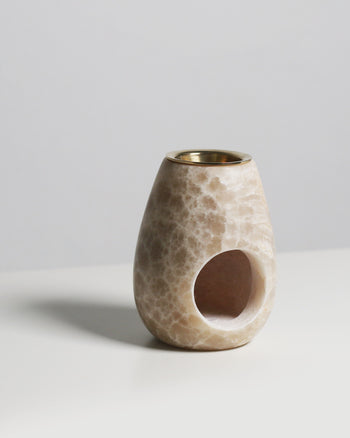 The stillgoods Eli Oil Burner is a marble-patterned, egg-shaped essential oil diffuser with a brass insert and side opening—ideal for adding calming scents to your space. It sits elegantly on a white surface against a light gray background.