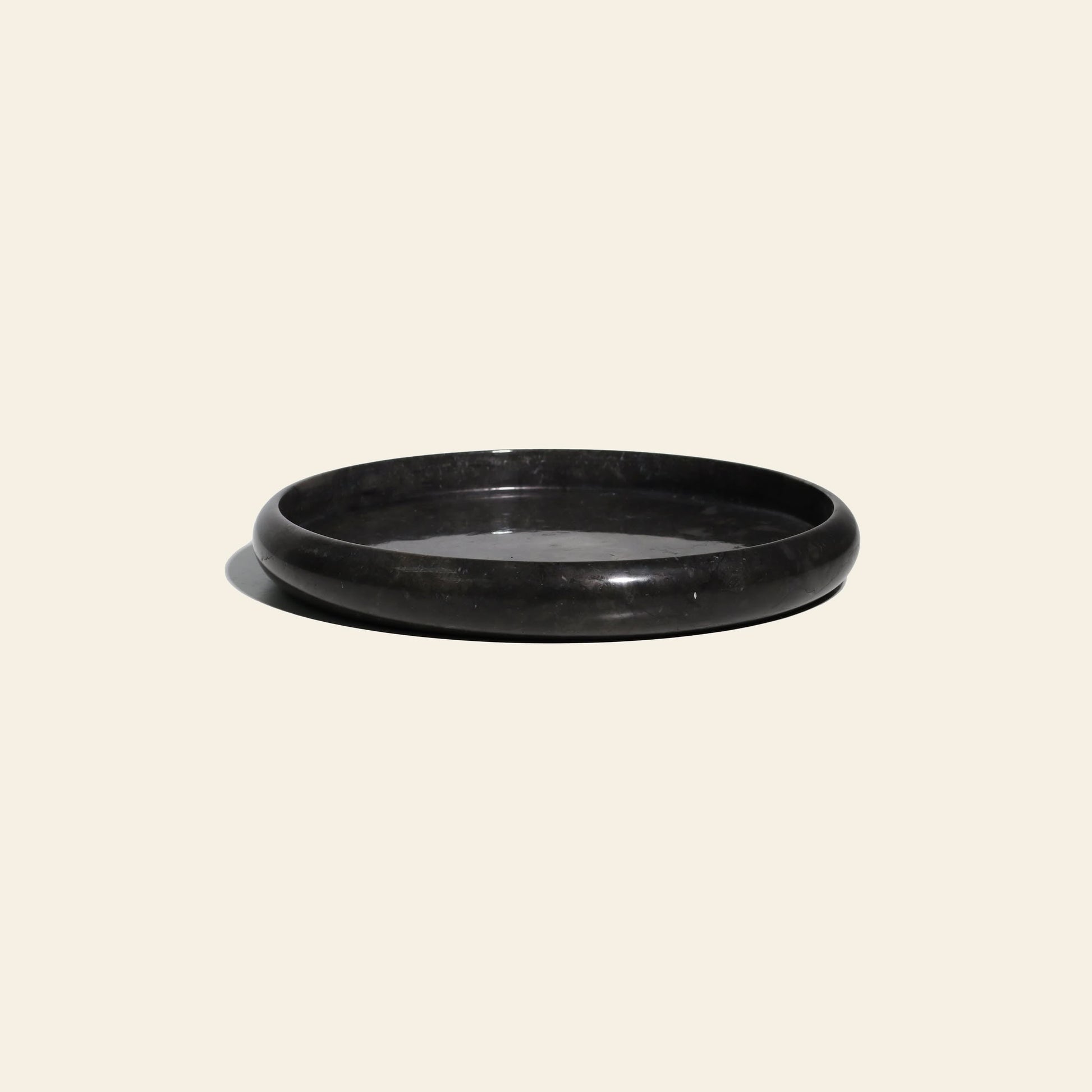 The stillgoods Harmony Tray is a black, round, low-profile tray with a smooth, glossy finish—ideal for displaying decor or serving as a marble centerpiece. Shown here against a plain cream background.