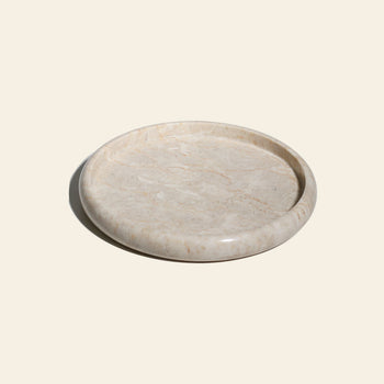 The stillgoods Harmony Tray is a round, flat beige marble tray with a raised edge. Its polished surface and natural veining make it perfect as a centerpiece or for displaying decor by stillgoods in any home setting.