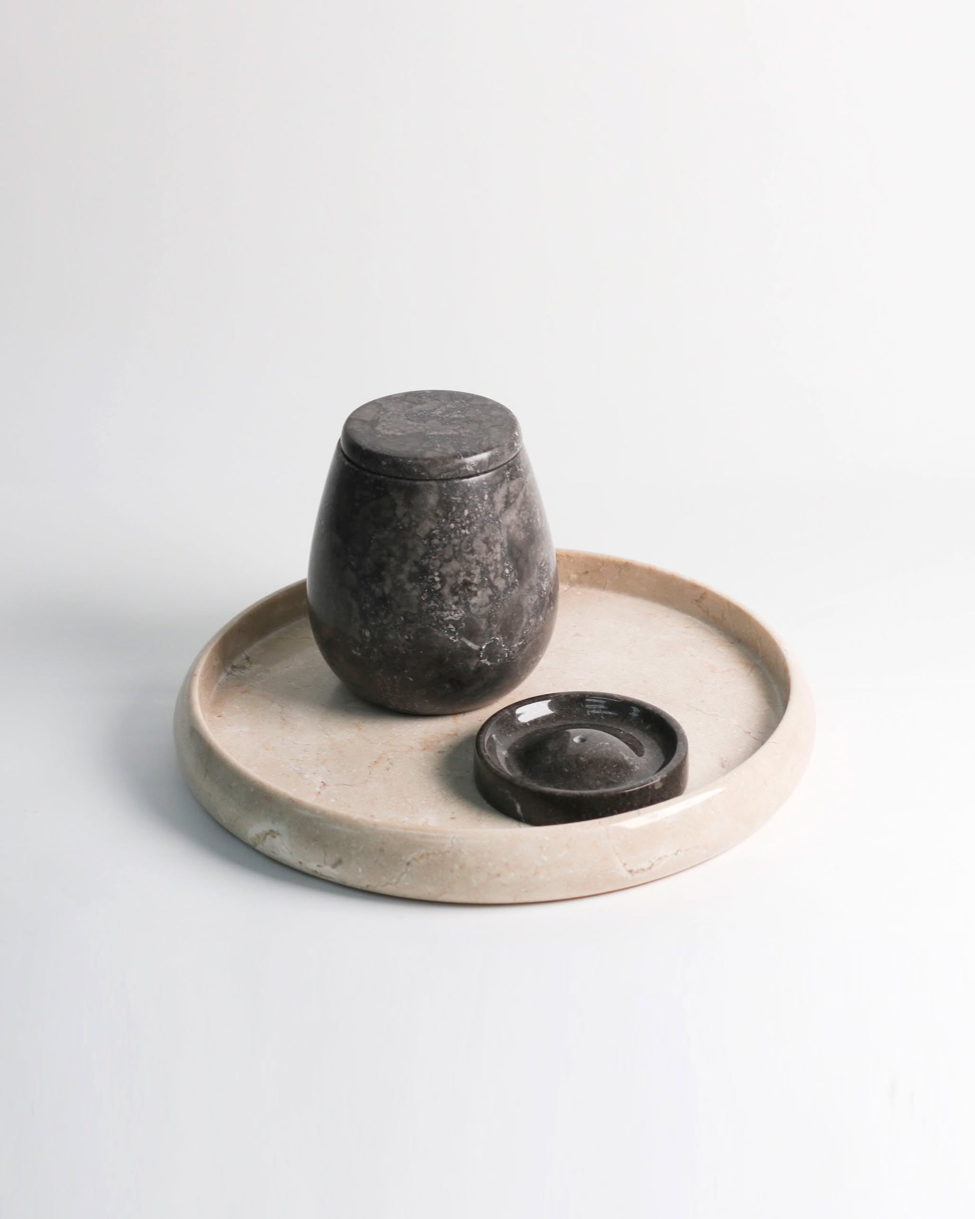 The stillgoods Harmony Tray by stillgoods features a dark, rounded stone jar with lid and a matching dish, all set on a light marble tray—an elegant centerpiece for modern home decor, shown against a plain white background.