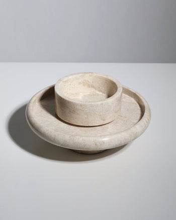 The stillgoods Harmony Tray by stillgoods is a round beige marble centerpiece dish with a raised central bowl and wide flat base, adding elegance to your decor. Shown on a white surface with a plain light gray background.