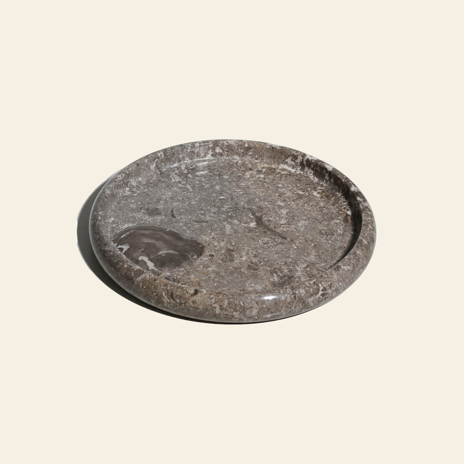 The stillgoods Harmony Tray by stillgoods is a round, shallow gray stone tray with a polished finish and natural patterns—an elegant centerpiece ideal for displaying decor or enhancing your home style.