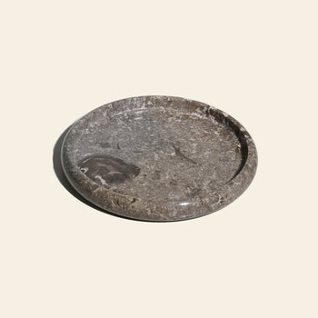 The stillgoods Harmony Tray by stillgoods is a round, shallow gray stone tray with a polished finish and natural patterns—an elegant centerpiece ideal for displaying decor or enhancing your home style.